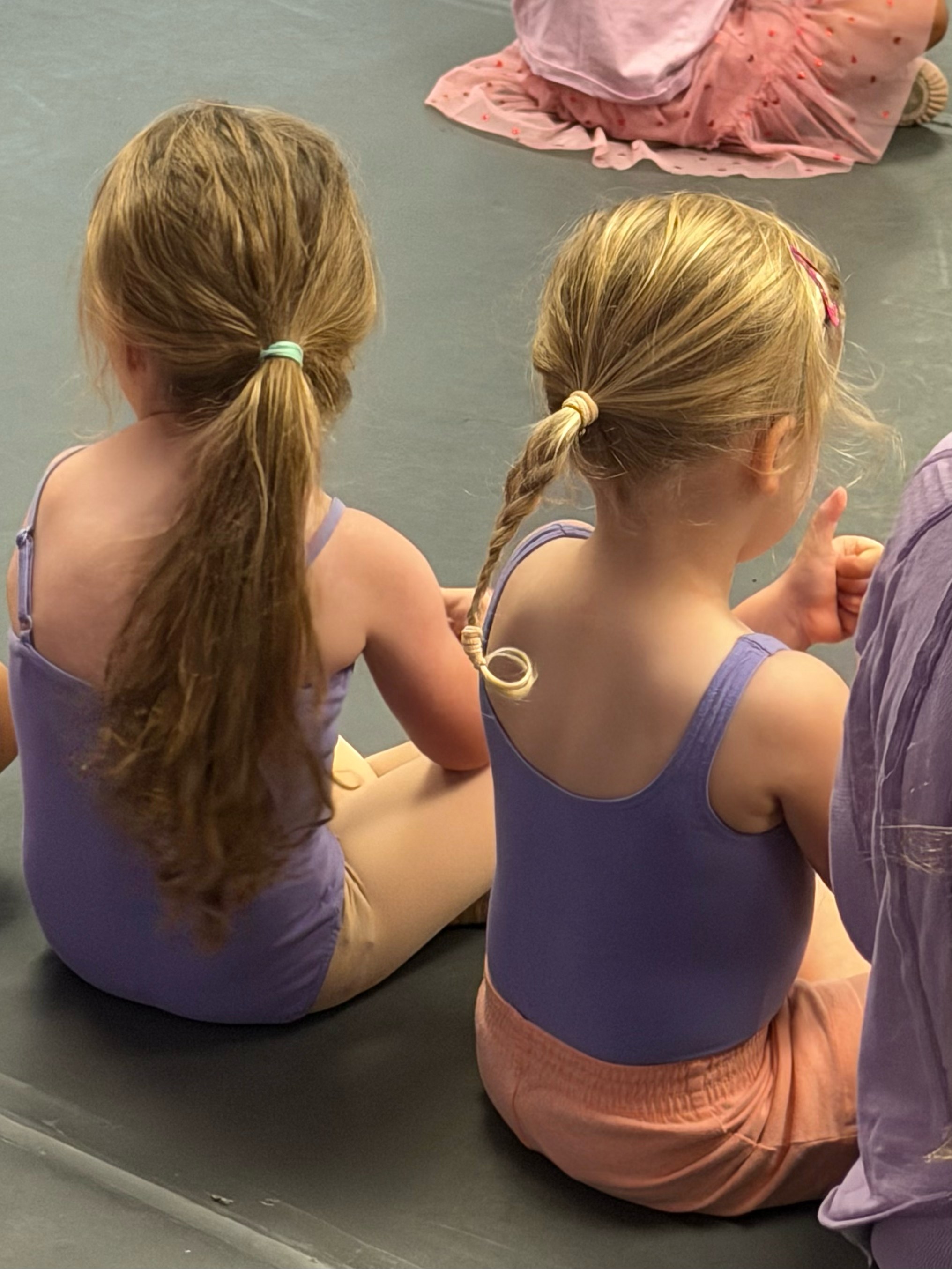 Two young dancers in purple leotards sitting together during class